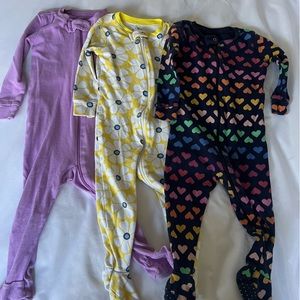 Primary onesies in colorful heart print, yellow with floral pattern, and purple
